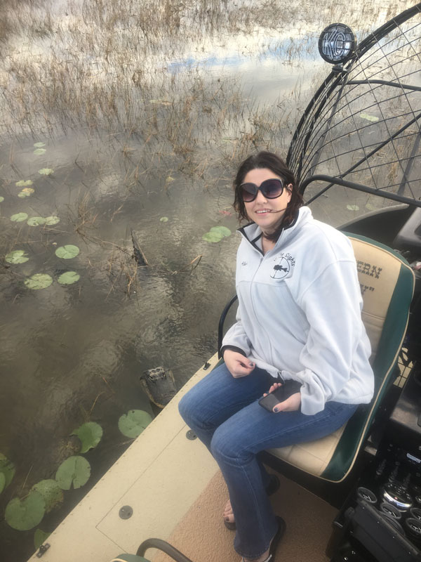 image of woman on airboat with alligator swimming in water next to her